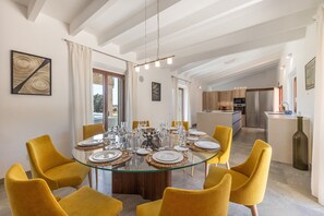 Ein modernes Esszimmer mit einem Glastisch, gelben Stühlen und einer Küche im Hintergrund.