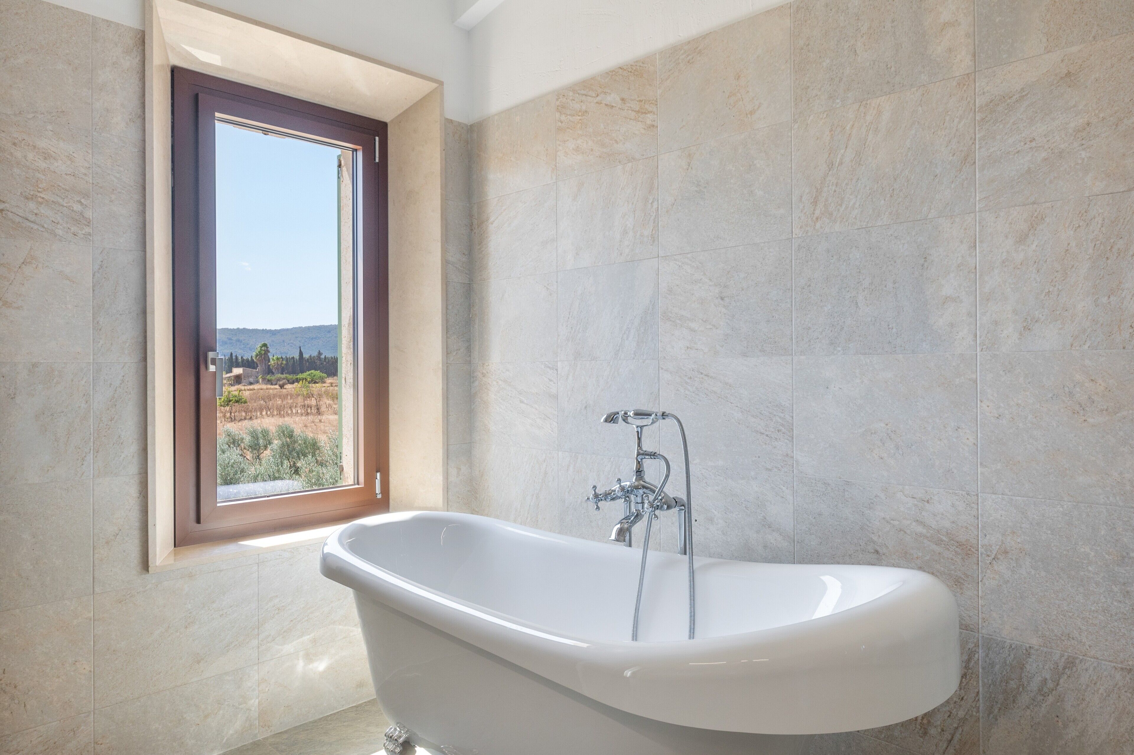 Ein Badezimmer mit einer freistehenden Badewanne, einem Fenster mit Blick auf eine Landschaft und gefliesten Wänden.