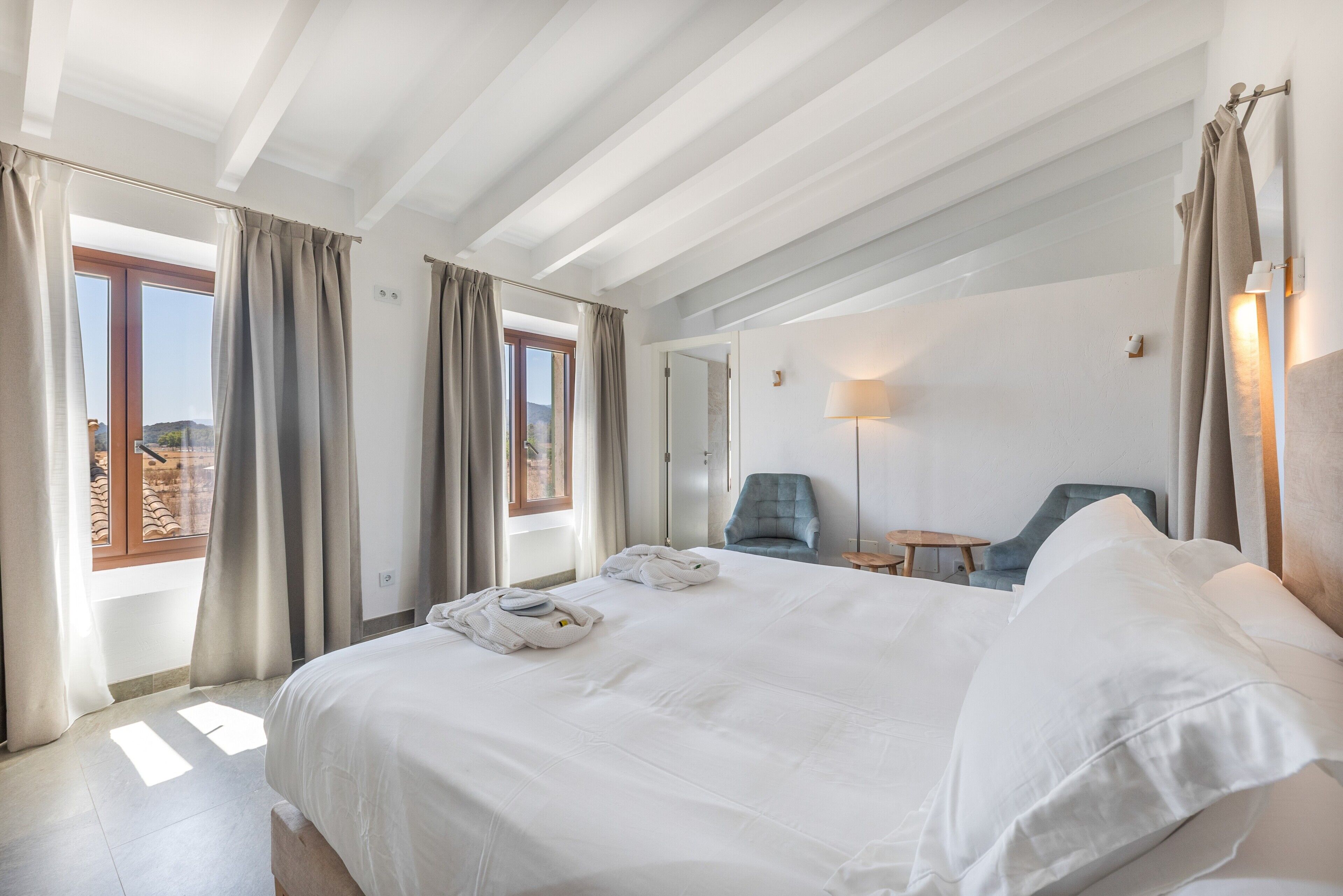 Hotellihuone, jossa on suuri sänky, tuoli, pieni pöytä ja peili.
