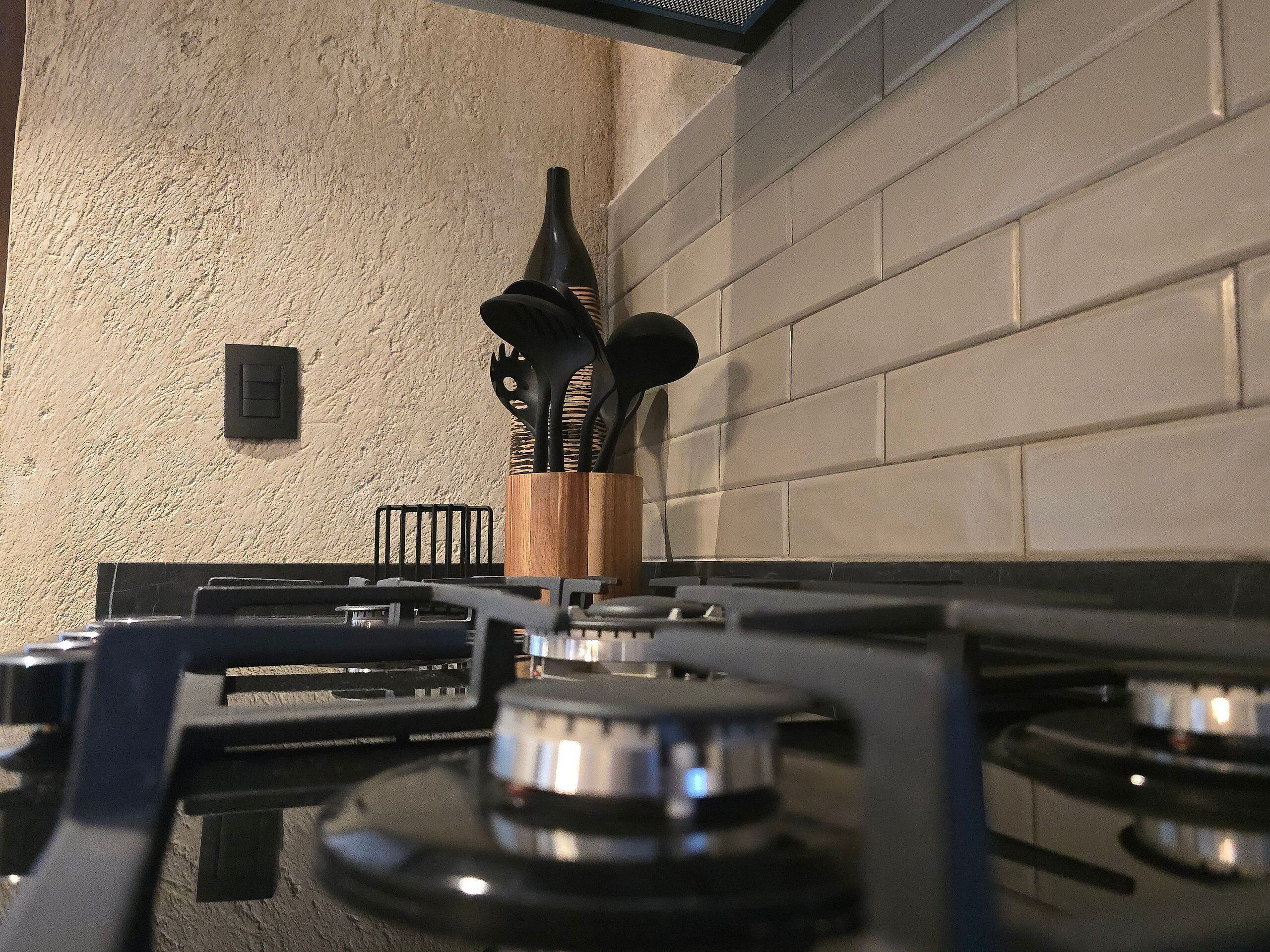 Une cuisine équipée d’une cuisinière à gaz, d’un porte-ustensiles en bois et d’un mur à texture.