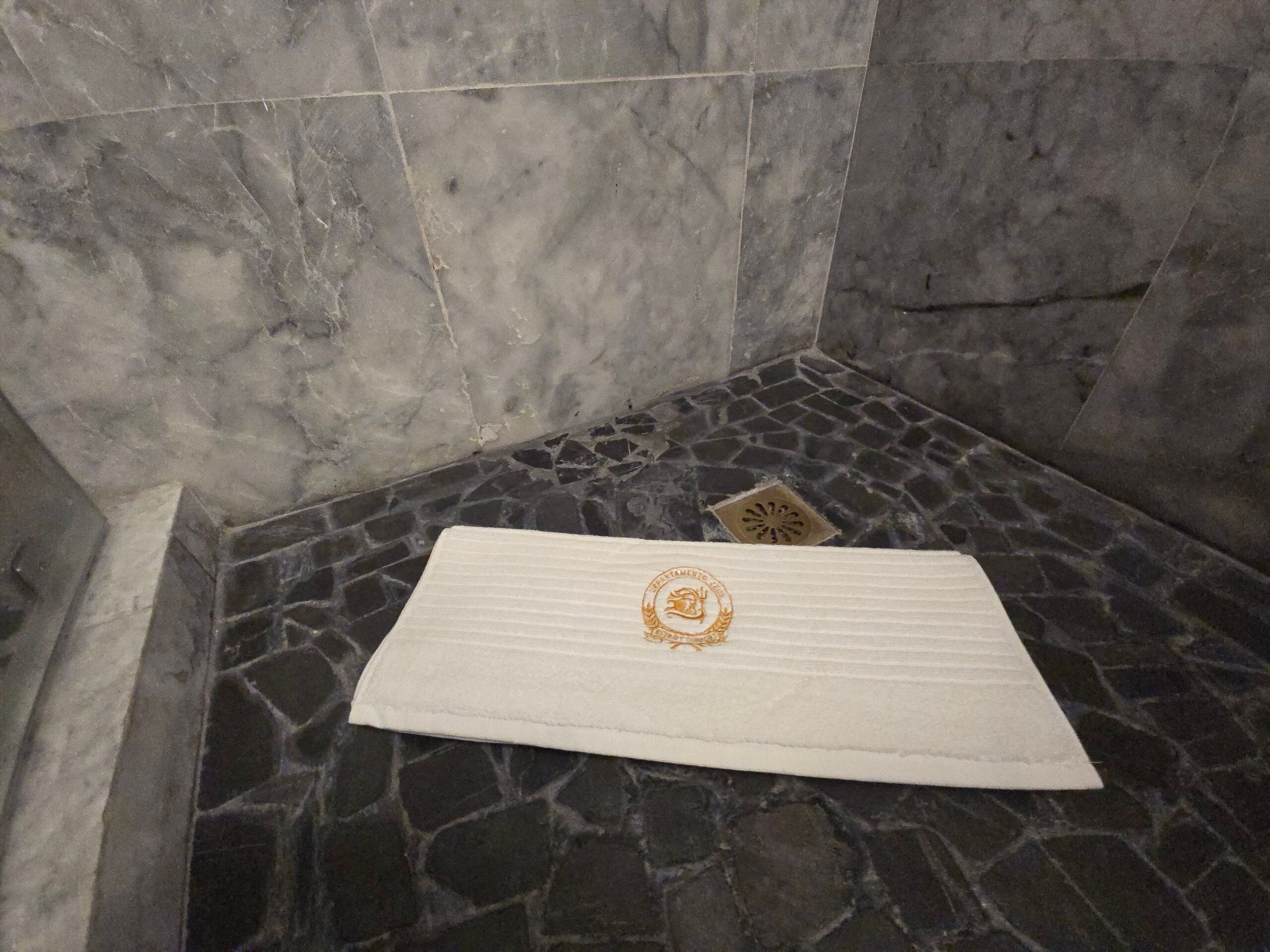 A bathroom with a stone floor, a white towel, and a drain.