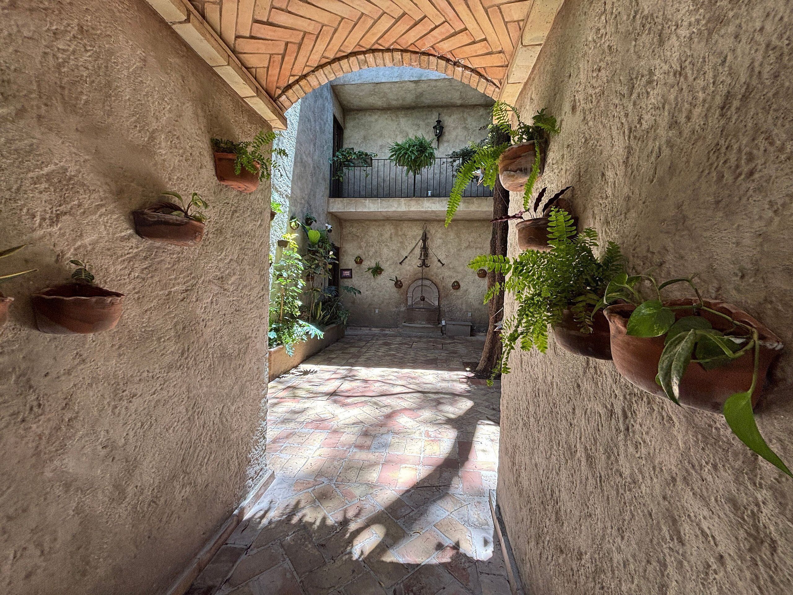 Un cortile stretto con piastrelle in terracotta, piante in vaso e un arco in mattoni.
