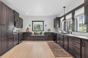 A modern kitchen with dark wood cabinets, a built-in bench with cushions, a large window, and a view of greenery outside. - Group Retreat Near Glacier | Lake Views (Somers)