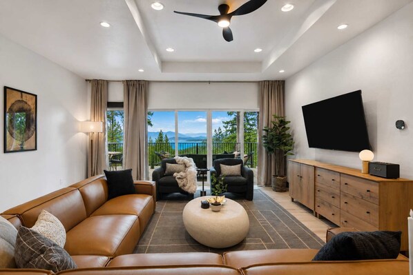 A modern living room with a sofa, chairs, a coffee table, a TV, and a balcony with a view. - Group Retreat Near Glacier | Lake Views (Somers)
