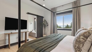 A modern bedroom with a bed, a TV, a window with a view, and a plant. - Group Retreat Near Glacier | Lake Views (Somers)