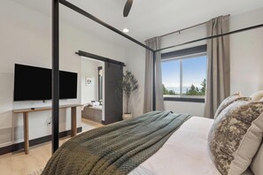 A modern bedroom with a bed, a TV, a window with a view, and a plant. - Group Retreat Near Glacier | Lake Views (Somers)