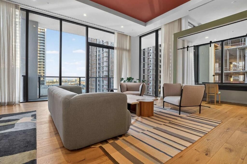 A modern living room with a sofa, armchairs, a coffee table, and a view of a cityscape through large windows.