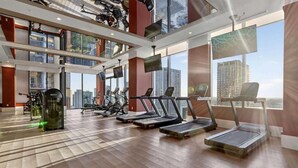 A gym with treadmills, stationary bikes, and weight machines, large windows with a city view, and a high ceiling. - The Crosby Miami Worldcenter (Miami)