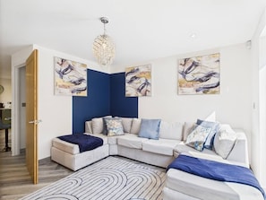 A modern living room with a sectional sofa, a decorative chandelier, and abstract wall art.