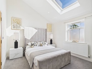 A bedroom with a skylight, a bed with a headboard, bedside tables, and a window with a view.