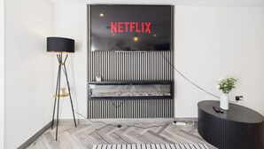 Un interior modern amb un senyal de Netflix, una làmpada de peu, una console i una catifa amb dibuixos.