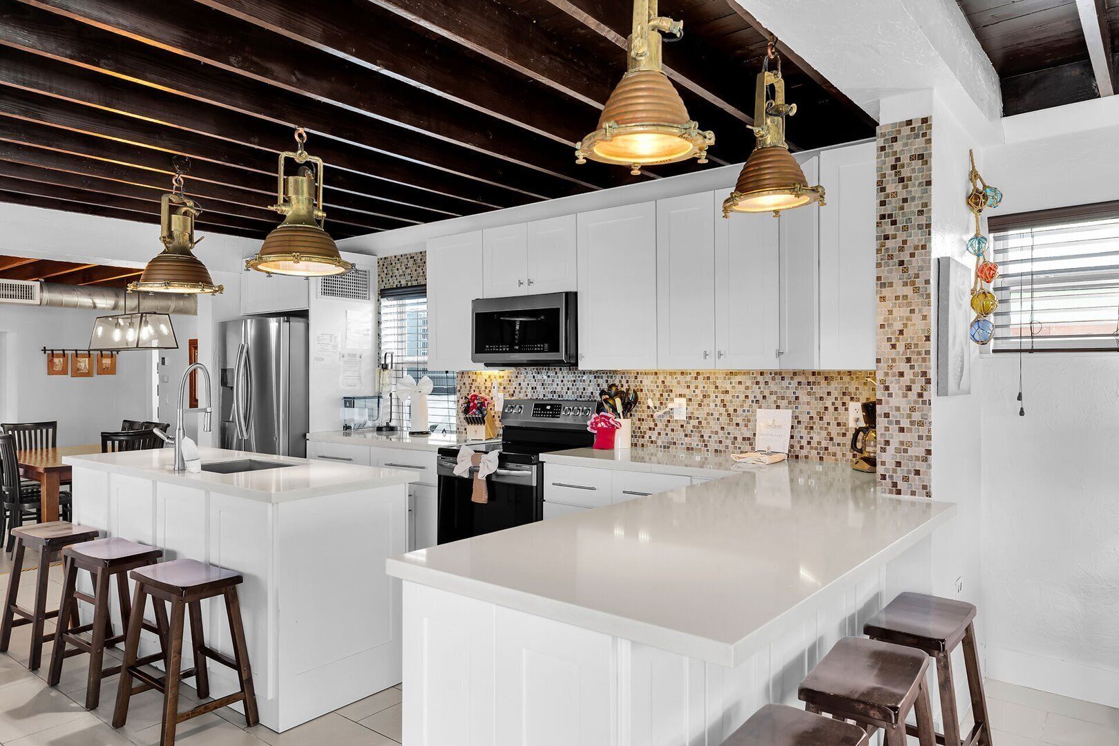 A modern kitchen with white cabinetry, a large island, bar stools, and pendant lighting.