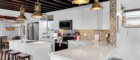 A modern kitchen with white cabinetry, a large island, bar stools, and pendant lighting.