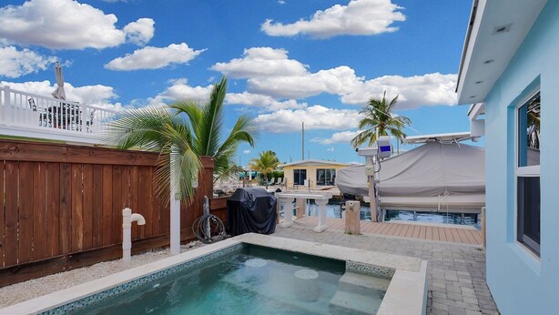 A swimming pool with a wooden fence, palm trees, and a covered area with a white umbrella. - La Pirata: Hgtv-Remodeled 3BR/2BA Canal Home w/ Pool (Marathon)
