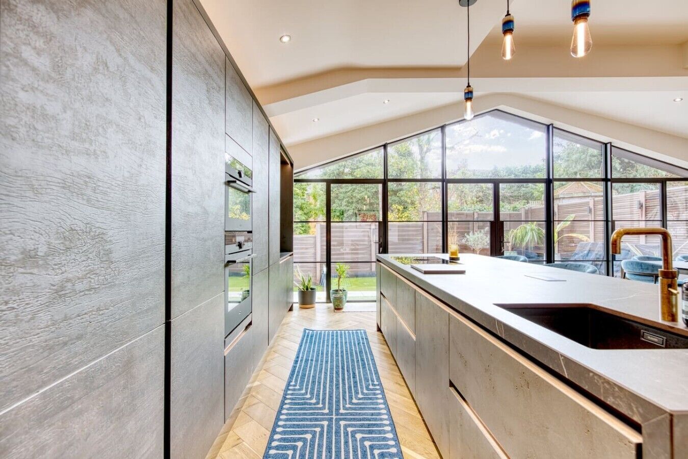 Una cucina moderna con un'isola grande, elettrodomestici integrati e vista sul giardino retrostante attraverso ampie finestre.