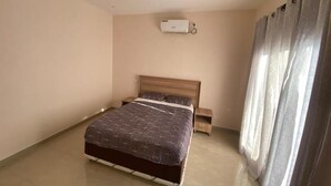 Un dormitori amb llit, una tauleta de nit, aire acondicionador fixat a la paret i una finestra amb cortines.