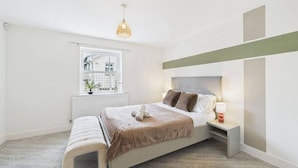 Ein Schlafzimmer mit Bett, Nachttisch, Lampe, Fenster und Ausblick nach draußen.