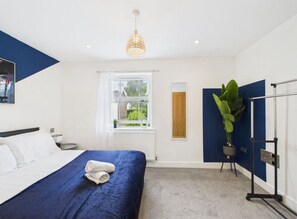 A modern hotel room with a large bed, a window with a view, a plant, and a radiator.