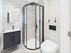 A modern bathroom with a glass-enclosed shower, a white toilet, a dark cabinet, and a mirror with a light strip. - Pristine Home • Near Station, Pantiles & Calverley (Royal Tunbridge Wells)