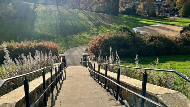 Steine Stufen führen zu einem Park mit Blick auf einen Golfplatz und Häuser in der Ferne.