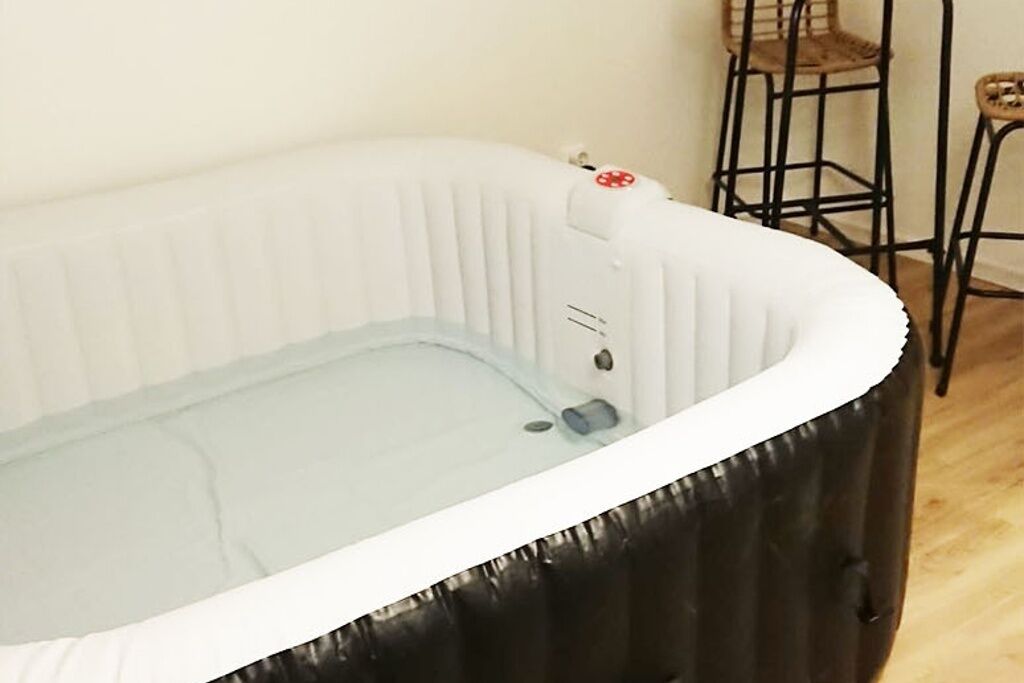 A white hot tub with a control panel, located in a room with a wooden floor and metal chairs.