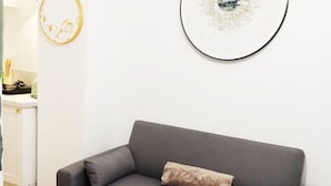 En grå soffa med en brun kudde, ett vitt, runt bord och två konstverk som hänger på väggen.
