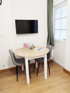 Ein Essbereich mit einem runden Tisch, zwei Stühlen, einem flachbildfernseher an der Wand und einem Fenster mit Vorhang.