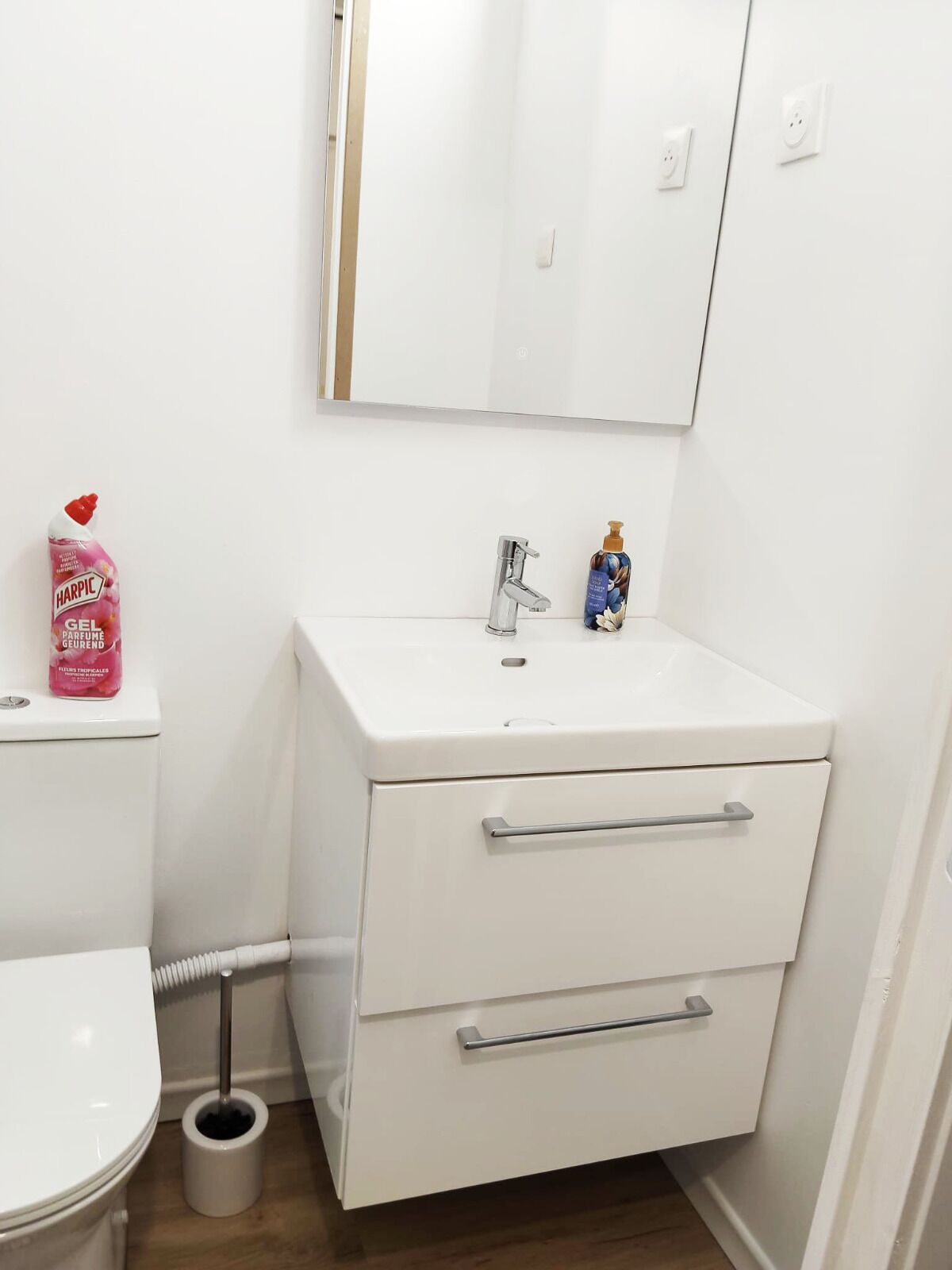 Une salle de bain blanche avec des toilettes, un bidet et un lavabo surmonté d’un miroir. On trouve des articles de toilette sur le lavabo.