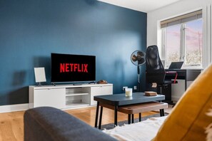 Ein Wohnzimmer mit Fernseher, der 'NETFLIX' anzeigt, einem Ventilator, einem Laufband und einem Fenster mit Blick.