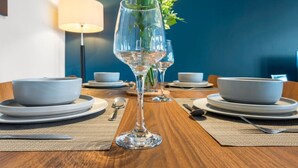 Una mesa de comedor con platos, cubiertos, una copa de vino y un florero con flores.