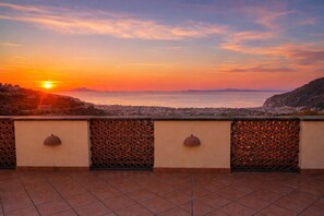 Une terrasse offrant une vue sur le coucher de soleil sur la mer, un sol carrelé et un mur décoratif orné de motifs circulaires.
