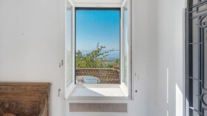 Una habitación con ventana que da a un balcón con vistas al mar y árboles.