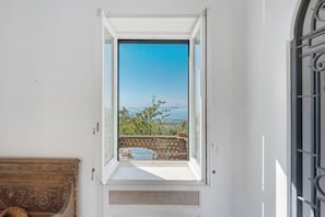 Una stanza con una finestra che si affaccia su un balcone e offre vista sul mare e sugli alberi.