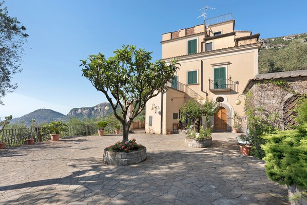 A building with a stone courtyard, potted plants, and a mountain in the background.