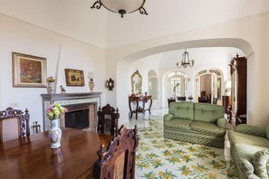 Une salle à manger avec une table en bois, des chaises, un vase de fleurs, une cheminée et un canapé vert.