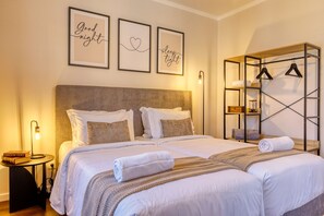 A double bed with white linens, a bedside table with books, and a wall-mounted shelf with hangers. - Freitas Panoramic, a Home in Madeira (Ponta do Sol)