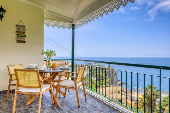 A balcony with a table and chairs, overlooking a coastal view. - Freitas Panoramic, a Home in Madeira (Ponta do Sol)