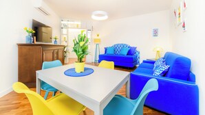 Un salon moderne avec un canapé bleu, une table à manger avec des chaises, un téléviseur et un coin cuisine.