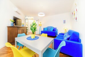A modern living room with a blue sofa, a dining table with chairs, a TV, and a kitchen area. - Cozy Apartment for Family in Sorrento City Center (Sorrento)