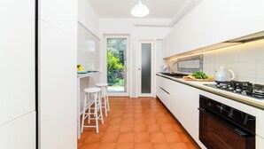 Une cuisine étroite avec des meubles blancs, une cuisinière à gaz et un petit coin repas équipé de tabourets.