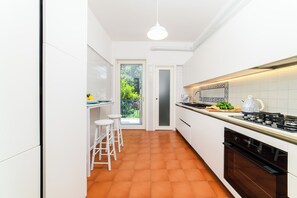 A narrow kitchen with white cabinets, a gas stove, and a small dining area with stools. - Cozy Apartment for Family in Sorrento City Center (Sorrento)