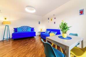 A modern living room with two blue sofas, a dining table with chairs, a potted plant, and a lamp. - Cozy Apartment for Family in Sorrento City Center (Sorrento)
