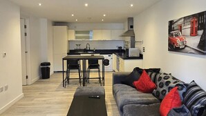 A compact living space with a kitchenette, a dining area, and a sofa with patterned cushions. - Canary Wharf 2BR | Skyline View + Work Ready (Greater London)