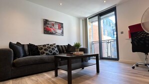 A modern living room with a sofa, a coffee table, and a painting of a car and telephone booth. - Canary Wharf 2BR | Skyline View + Work Ready (Greater London)