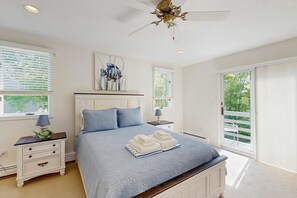 Ein Schlafzimmer mit Bett, Nachttischen, Deckenventilator und Blick durch das Fenster.