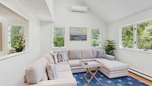 A modern living room with a sectional sofa, a small coffee table, and large windows with views of greenery.