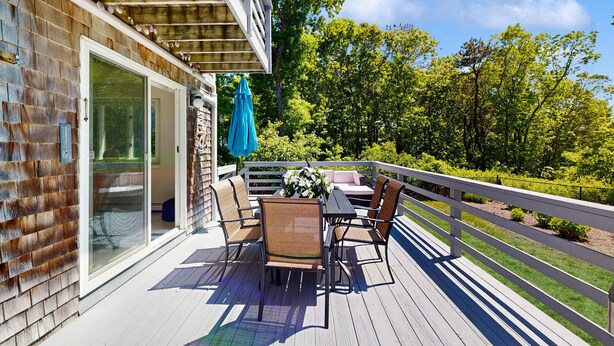 An outdoor deck with a table and chairs, a blue umbrella, and a white railing.