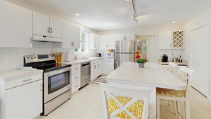 A modern kitchen with white cabinetry, stainless steel appliances, a central island with seating, and a view into the dining area.