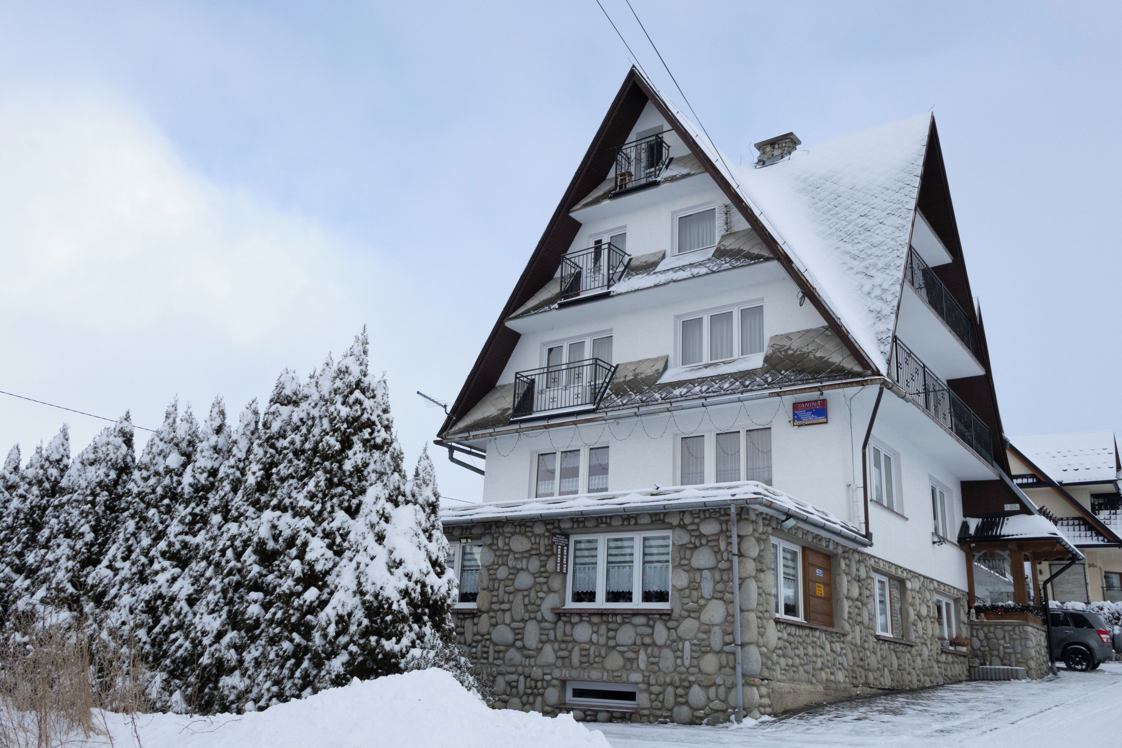 A multi-story building with a stone base and white upper levels, featuring balconies and a snow-covered roof.