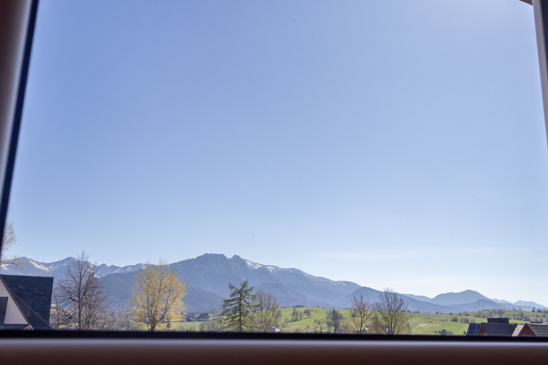 Blick durch ein Fenster auf eine Berglandschaft, im Vordergrund stehen Gebäude.